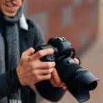 netter-junger-mann-betrachtet-fotos-der-kamera-gekleidete-warme-jacke-grauer-schal-scaled-aspect-ratio-1-1